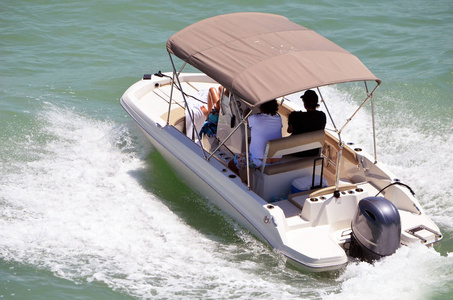 舵手和两名乘客享受高速旋转在一个小型机动船驱动的一个单一的舷外发动机的佛罗里达州沿海水路关闭迈阿密海滩, 佛罗里达州