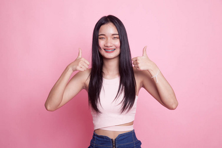 年轻的亚洲妇女在粉红色背景上显示两个大拇指