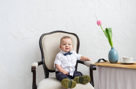 时髦的男婴坐在白色房间的扶手椅上。水平肖像