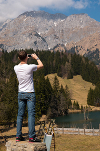 男人拍照的智能手机在阿尔卑斯山的小山湖的