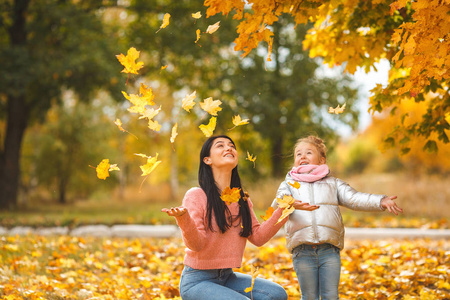 欢快的女孩玩黄叶。快乐的母亲和小孩子在秋天的时间有乐趣