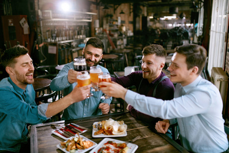 在酒吧喝啤酒的男人朋友们在酒吧里用酒精饮料干杯。高分辨率