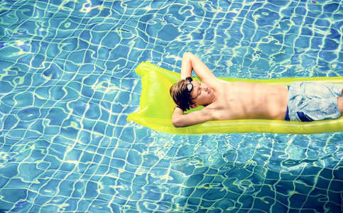 在游泳池充气床上享受漂浮的年轻高加索男孩