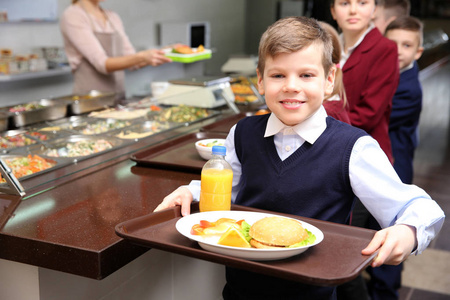 逗人喜爱的女孩拿着盘子与可口食物在学校自助餐厅