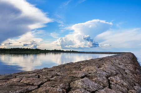 拉多加湖湖上的石坝码头。阳光明媚的夏日风景。蓝天和云彩反射在水面上