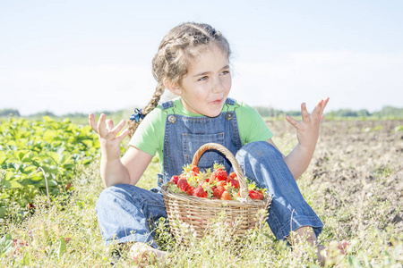 在夏日的花园里, 一个阳光明媚的日子, 一个小甜甜的卷发女孩吃草莓。