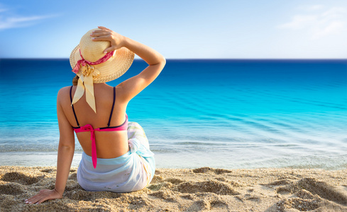 年轻女人享受坐在靠近海边的沙滩上的太阳
