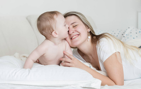 幸福微笑的年轻母亲的肖像躺在双床上的婴儿儿子