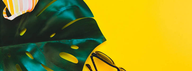 热带丛林棕榈龟背竹叶子, 太阳镜和妇女的泳装顶部在明亮的黄色纸背景。暑期创意平面布局概念模板的文本。长宽横幅