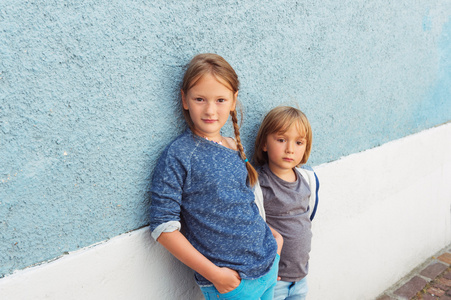 两个孩子，女孩和小男孩，在室外摆姿势，站在墙上蓝色
