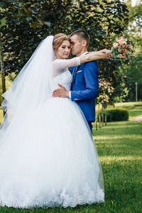 美丽的男人和女孩, 新娘在白色婚纱礼服, 新郎在经典的蓝色西装反对自然背景。婚礼, 家庭创造