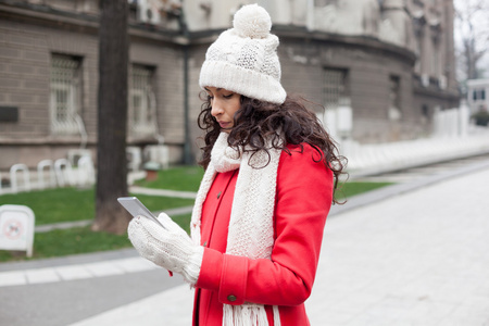 美丽的女人，在红色的外套和羊毛帽和手套 smartph