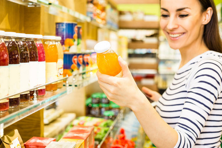 年轻的白种女人微笑从货架上选择超市的产品