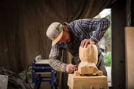 一个木匠的特写, 建筑工人在工作中锯出雕塑从木一个人的头在车间里, 周围有很多工具, 木制, 家具的工作