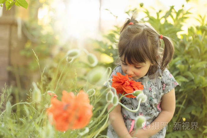 一个三岁小女孩的肖像在花园里闻花香