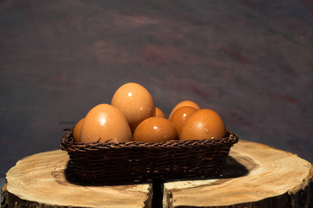 篮子鸡蛋在一个圆木桌上。美丽的黑暗背景