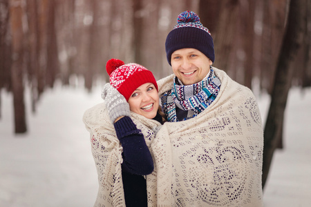 一对情侣在冬季公园散步。情侣们盖一条毯子