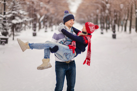 男人微笑着上升她女人戴着帽子和围巾在白雪皑皑的冬季公园拥抱