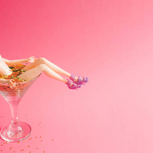 女性娃娃沐浴在马提尼玻璃充满金色闪光的粉红色背景, 创意极小的美丽夏日概念