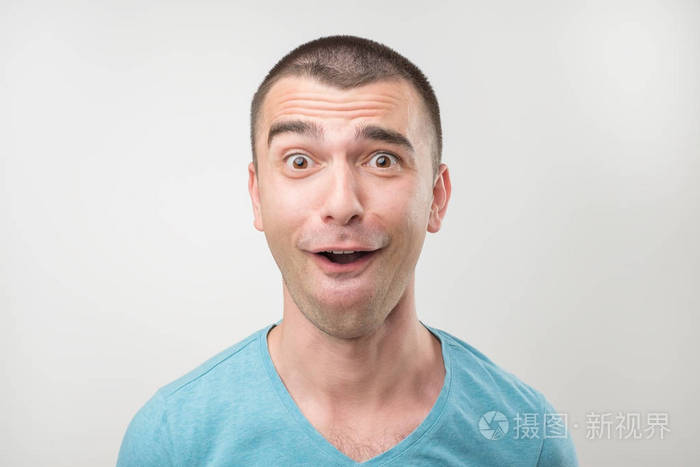 惊讶的年轻男子在马球 t恤上灰色背景.特写面部表情