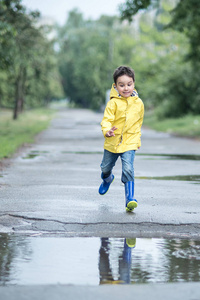小男孩在雨衣和橡胶靴在水坑里玩
