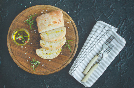 切片 ciabatta 面包与橄榄油和迷迭香在木板上的黑暗石背景。意大利食物概念。顶部视图