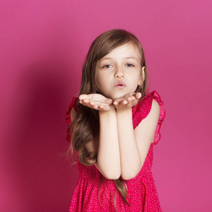 8岁的小女孩在粉红色的中性背景下, 用手做一些情绪化的手势。她有长黑发和穿红色夏天礼服。她脸上的滑稽表情