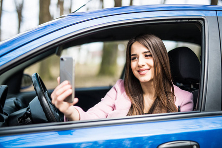 微笑的年轻女士带户外在汽车智能手机相机自拍照图片