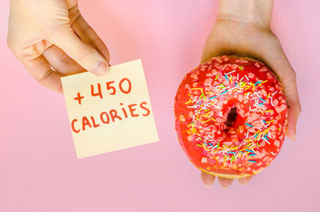 妇女手拿着粉红色的甜甜圈与洒额外的卡路里脂肪快餐过量体重不健康的黄色背景