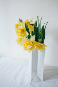 水仙花的纸袋的花束。鲜花递送。黄色的春天的花朵。复活节的花束。生态包装。花园里的花。在桌子上的花。白表。民族风格。出售的鲜花