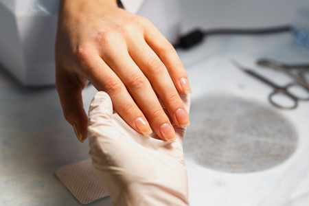 修指甲护理程序，特写照片的美容师手归档指甲的女人在沙龙