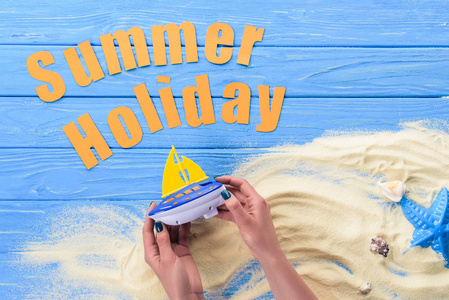 女性手用玩具小船由夏天假日题字在蓝色木背景