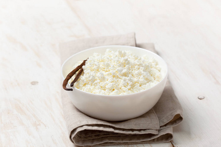 新鲜自制的平房奶酪在一个白色的碗, 香草荚白色木质背景