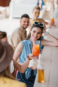 微笑的年轻妇女喝夏天鸡尾酒与朋友在海滩酒吧