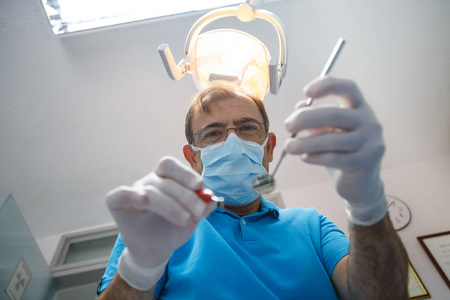 从下面的人拍摄的制服和手套使用工具和做口腔检查在牙科柜