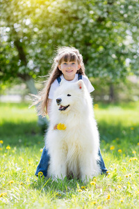 在公园里有一只大白狗的小女孩。一个美丽的5岁女孩在牛仔裤拥抱她最喜欢的狗在夏季散步