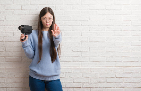 年轻的中国女子拍摄手持摄像机与张开手做停止标志认真和自信的表达, 防御姿态