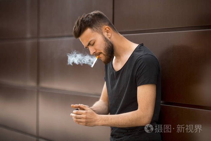 春天 一个穿着黑色 t恤衫的年轻英俊的白胡子男子在街上抽烟.特写