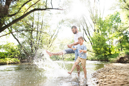 年轻的父亲与小男孩在河里，阳光明媚的春天的一天