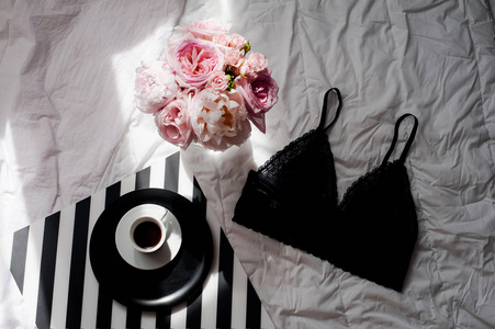 平躺。顶部查看黑色蕾丝内衣。美丽的博客概念。玫瑰和介子的花束, 咖啡在白色床背景