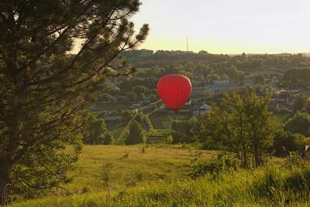 红气球飞过一个村庄, 位于风景如画的山丘之间。晴朗的蓝天上没有云彩, 在日落期间。乌克兰基辅地区