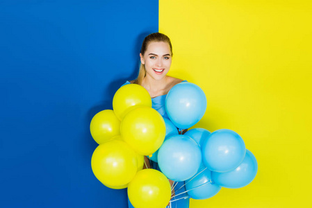 在蓝色和黄色背景下举行派对气球的女性时装模特
