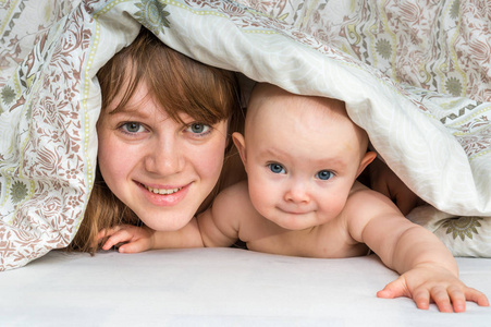母亲和她的孩子玩，在一条毯子下微笑