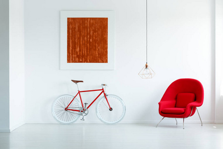 红色自行车旁边的扶手椅在最小的白色公寓内部与绘画和灯。真实照片