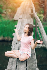 美丽的女人坐在一座木桥上, 微笑着。瑜伽, 自然, 健康概念