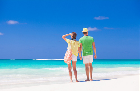 在明亮的衣服和帽子在热带海滩散步的夫妇