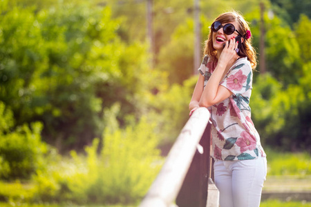 快乐的女人在公园里站在木桥上讲手机和笑