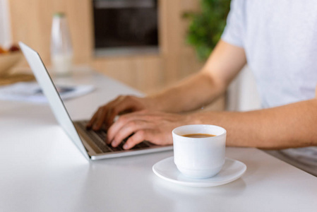 咖啡杯与男性在餐桌上使用笔记本电脑的选择性聚焦