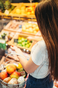 女性顾客与篮子反对果子部分在食物商店。超级市场的妇女购物