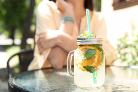 梅森罐子, 桌上放着可口的柠檬水, 还有在户外咖啡馆的少妇。天然排毒饮料